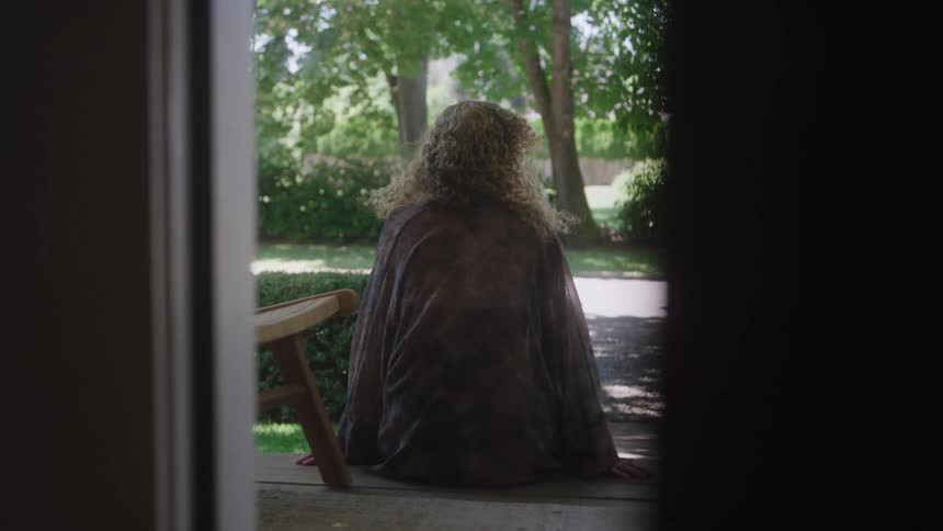 A young woman sitting outdoors at a home entrance during daytime