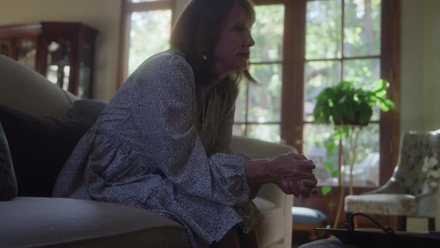 Woman sitting on the couch with her head resting on her hand appearing to be in reflection