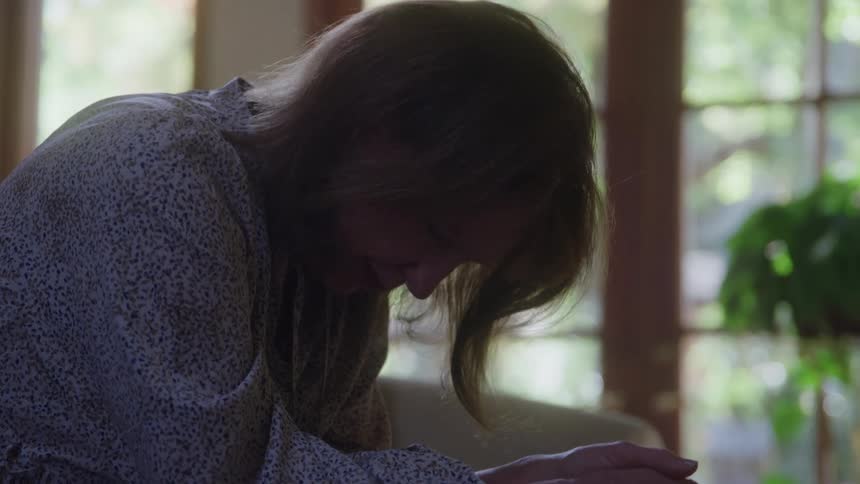 Close up of a middle aged woman crying while sitting on a couch in a room during daytime