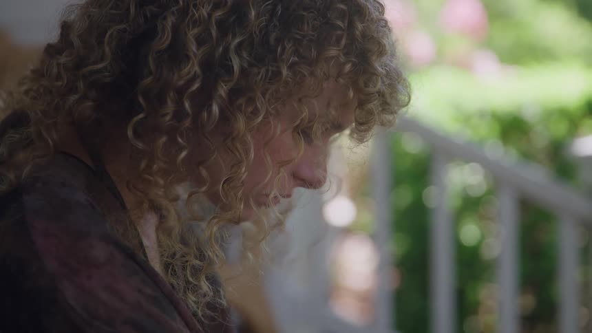 Woman with curly blonde hair looks downward