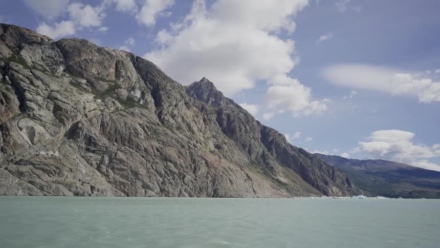 Lake waters flowing next to mountains on cloudy day