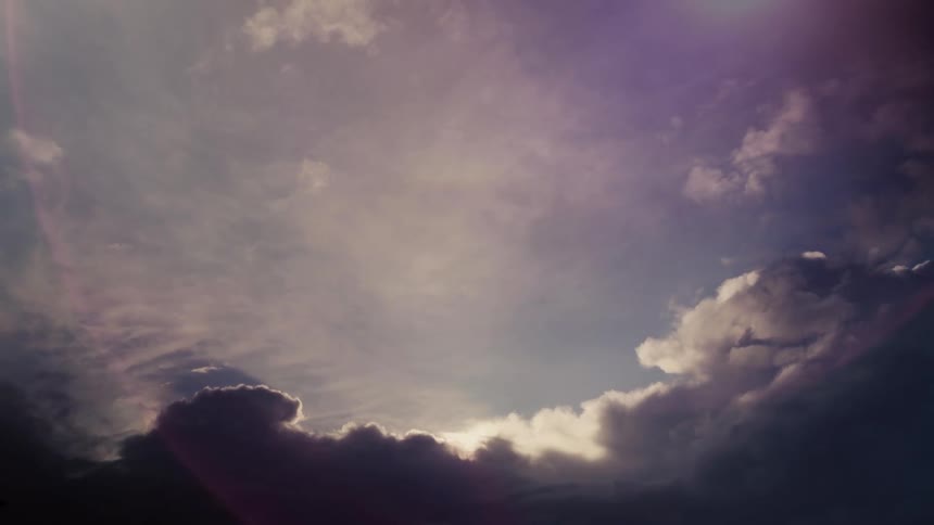 A low angle time lapse view shows dark moody storm clouds moving across the sky revealing a bright center of light as the cloud formations change