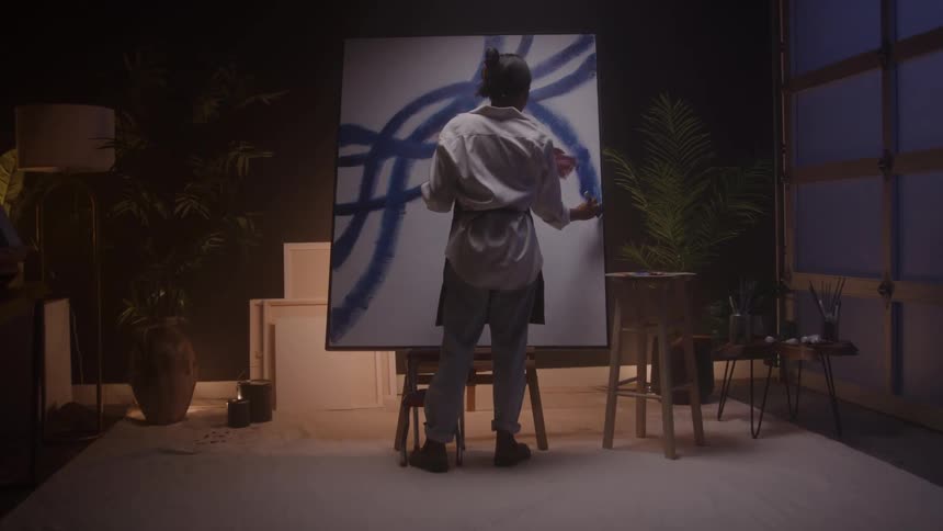 A young woman painting a large canvas while standing in a room