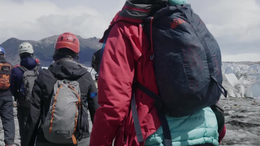 People wearing helmets and backpacks hiking up icy mountain side