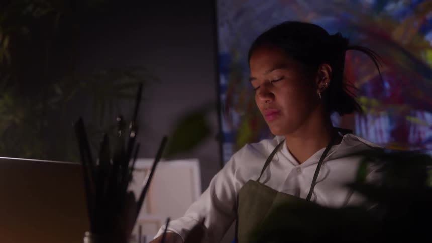 Close up of a female black artist painting a canvas in a room