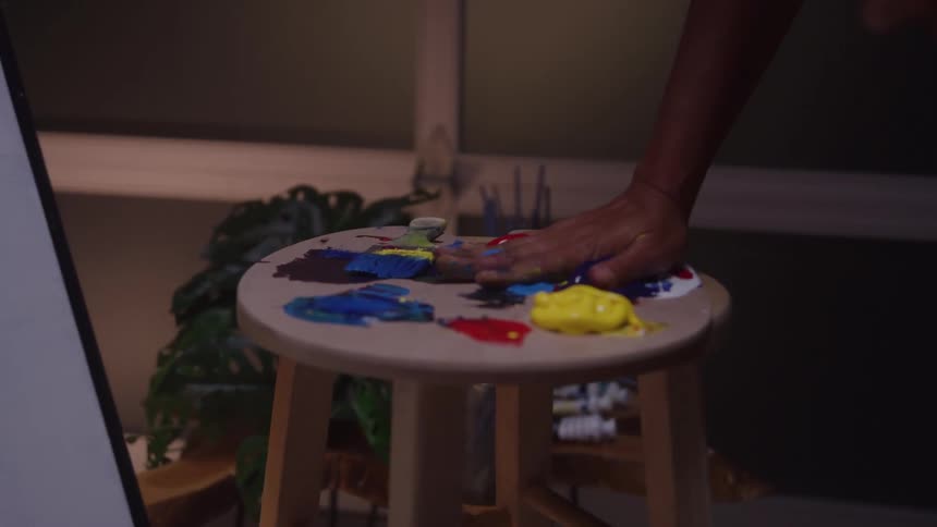 An artist in a studio rubs their hands into paint preparing to apply it directly onto the canvas before them