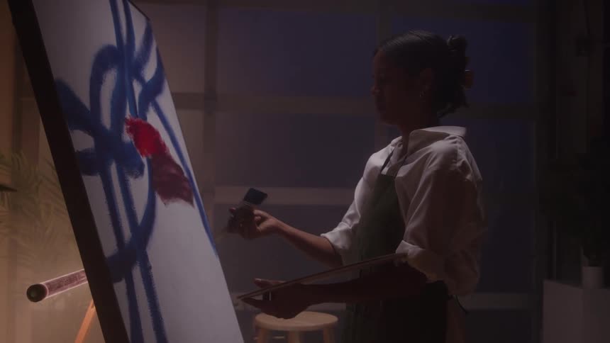 A young black female artist painting a large canvas in a room