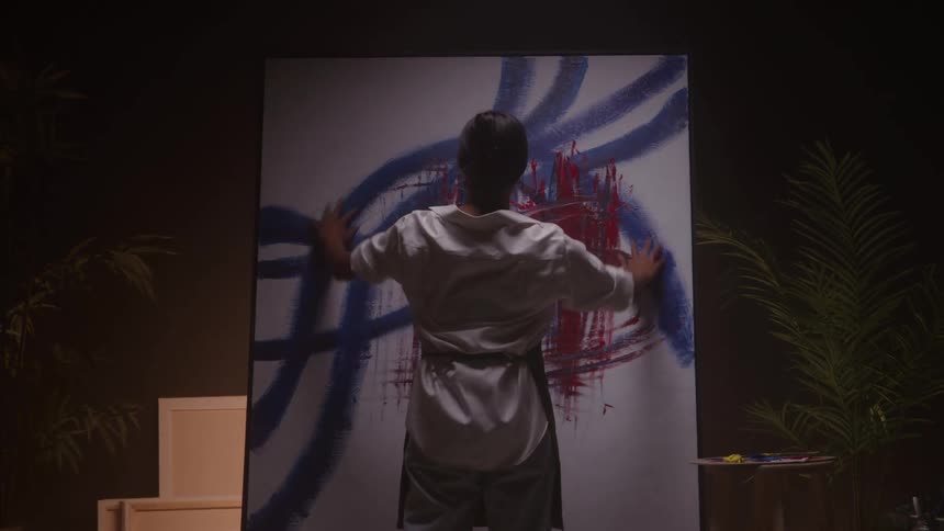 Woman applying paint with her hands onto a canvas with abstract blue and red strokes in a studio with art supplies