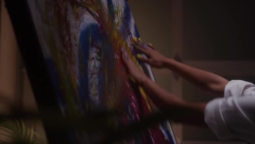 The woman wipes colorful paint on the canvas with her hands