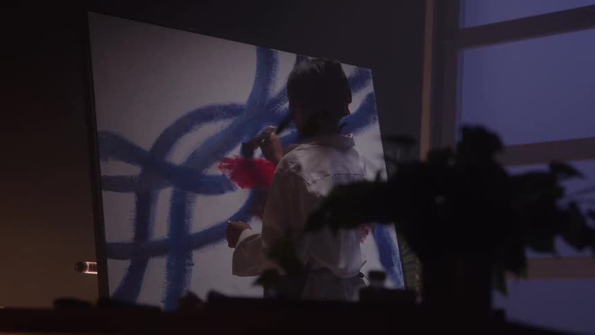 A woman paints on a canvas in a dim studio