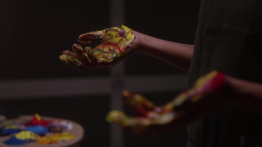 The artists hands are covered in different colored paints