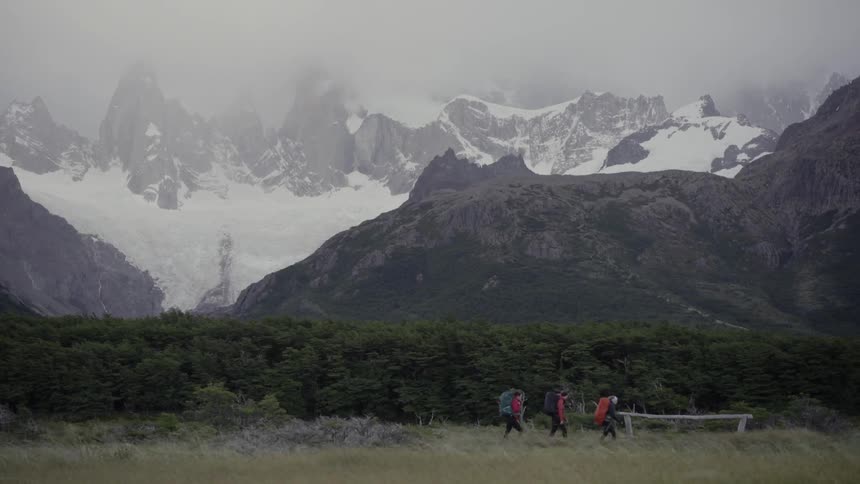 Hikers walk in a field with snowy mountains in the distance