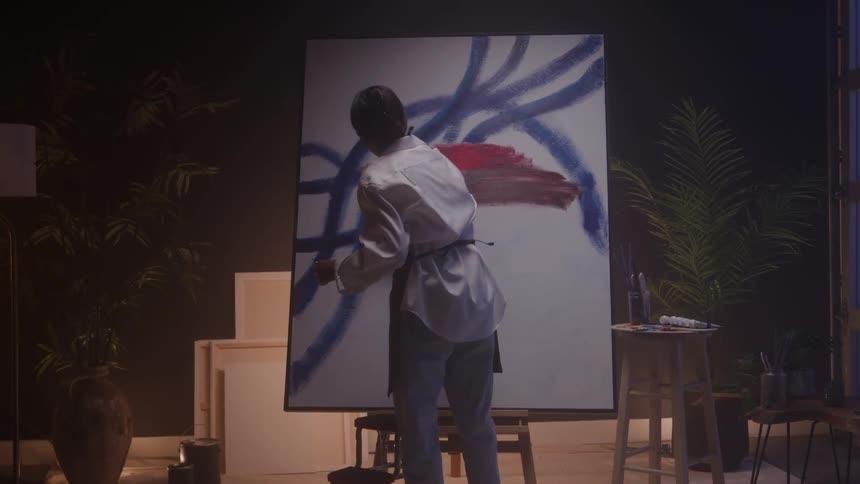 Woman painting abstract blue and red strokes on a canvas in a welllit studio with plants and art supplies in the background