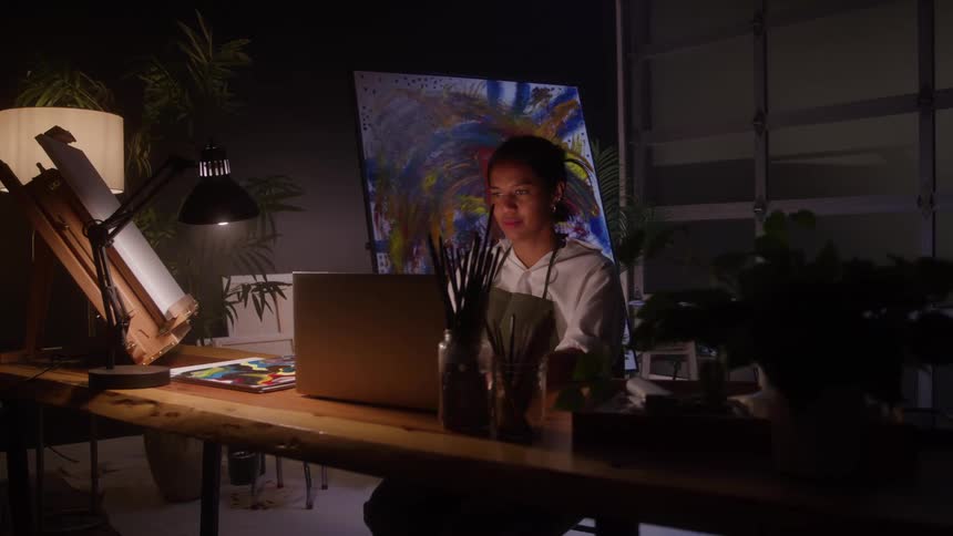 The woman sits at her laptop in the studio