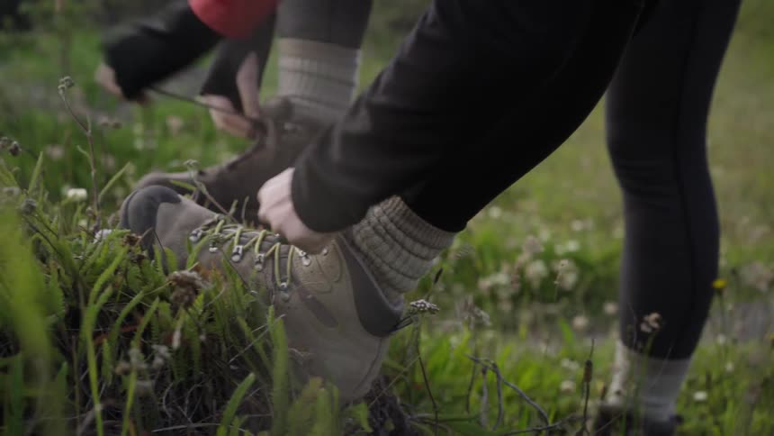 Two people tie their hiking shoes in a grass meadow