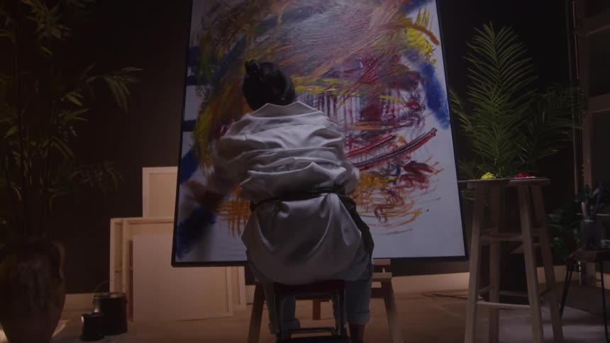 Woman painting a large colorful canvas in a lit studio