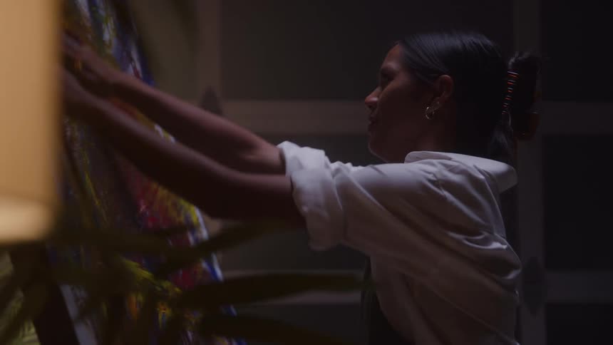 An artist in a studio rubs their hands into paint preparing to apply it directly onto the canvas before them