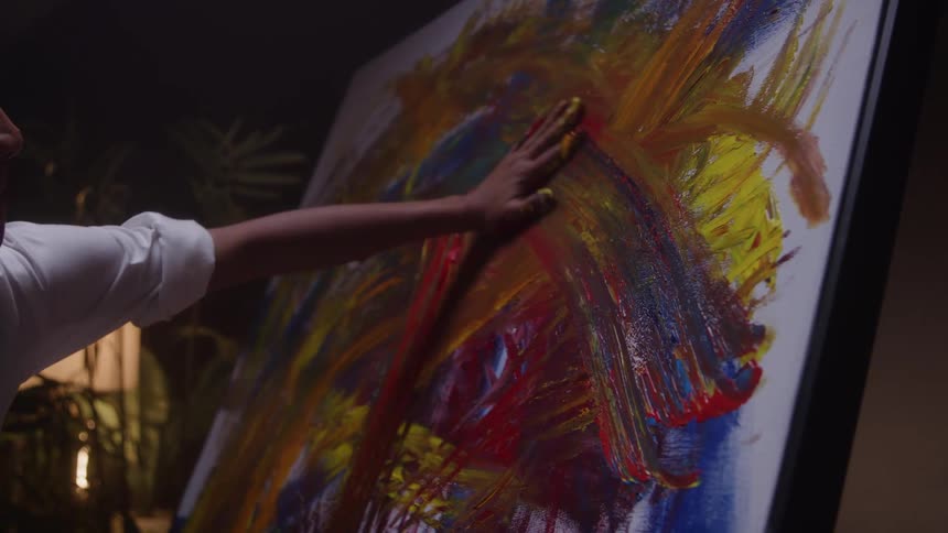 The video shows an artists hand vigorously applying thick vibrant streaks of paint directly onto a large canvas the colors are yellow red and blue creating a dynamic energetic field of abstract expression