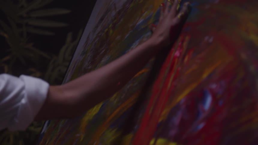 Woman touching vertical canvas with vibrant brushstrokes in red yellow blue and orange during artistic process