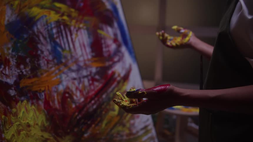 An artist stands in front of a painted canvas a fresh stain of color marking their palm as they pause in quiet reflection