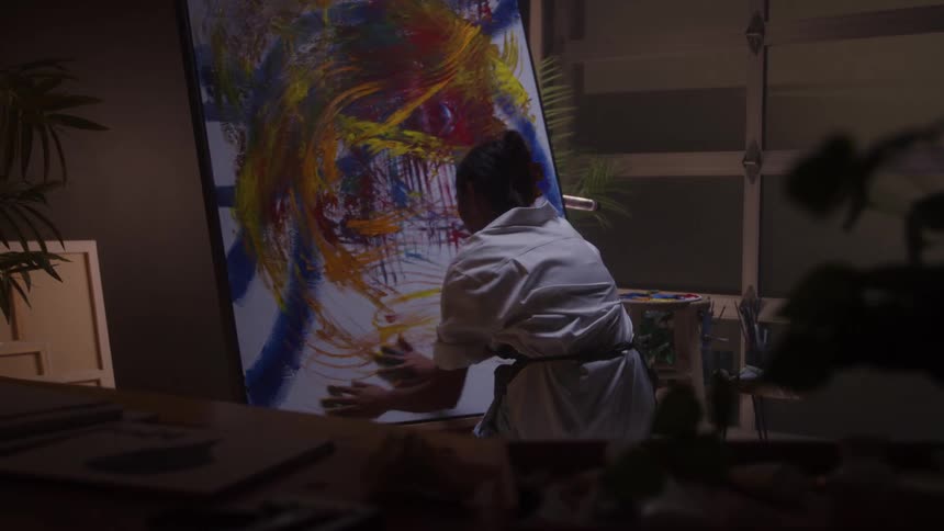 Artist paints with broad gestures on a large canvas filled with vibrant colors