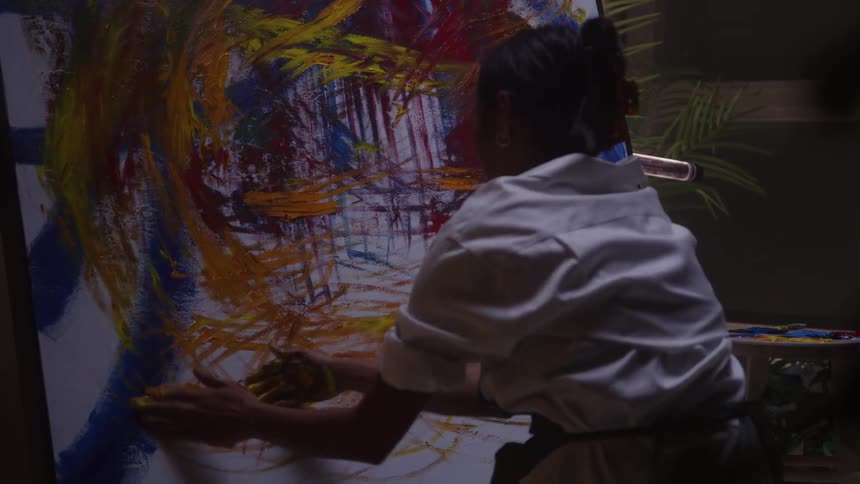 A female artist in a studio rubs paint from her hand onto a canvas crafting expressive artistic patterns through direct tactile strokes