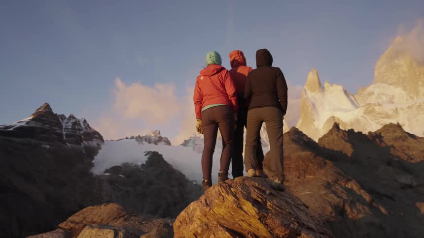 Three people perch on a rock on a mountain