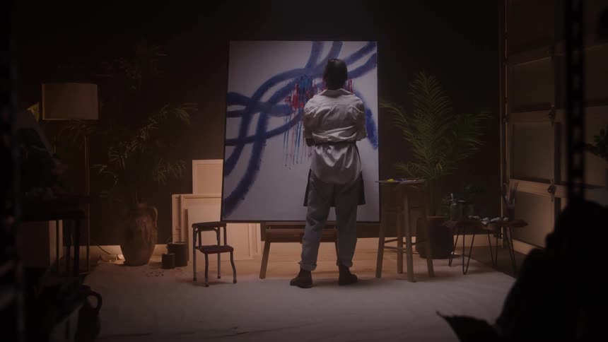 The artist is painting on the canvas streaking the red and blue paint
