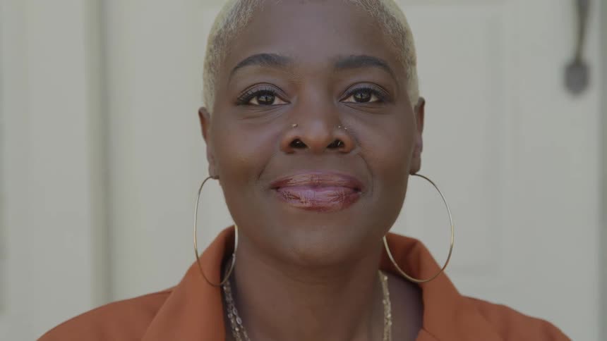 The video is a closeup of an african american woman with short bleached blonde hair and large gold hoop earringsshe is looking directly at the camera initially with her eyes closed before opening them and giving a slight confident smile