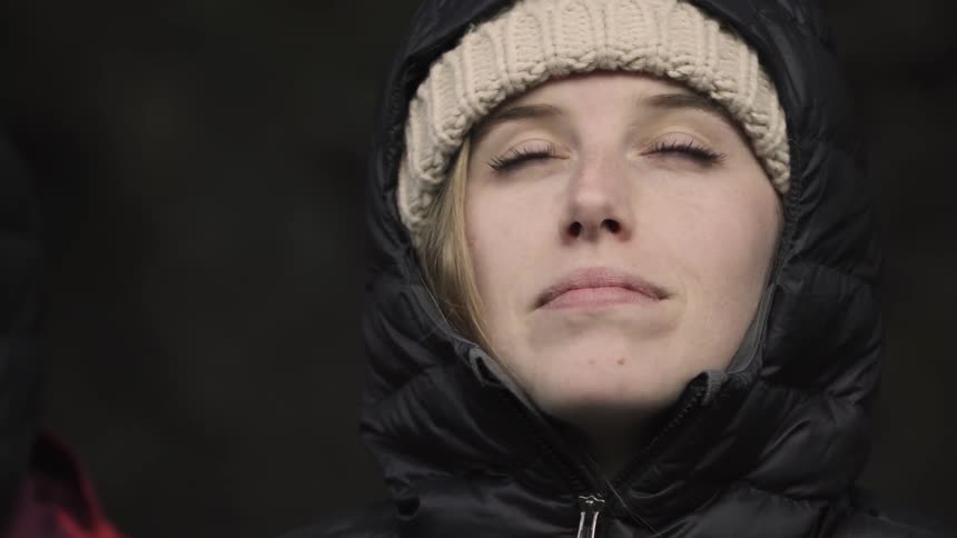 A woman wearing a coat and hat looks upward