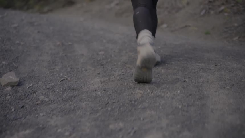 A person wearing sneakers walks on a dirt and gravel trail