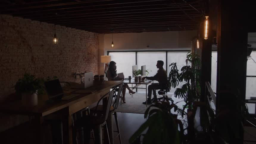 A man and a woman sit across from each other in an office during a midday interview session engaged in focused conversation under the natural light filtering through the windows