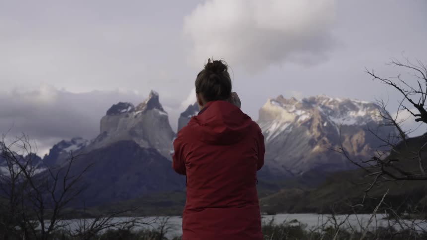 Woman taking photographs of snowy mountains on cloudy day