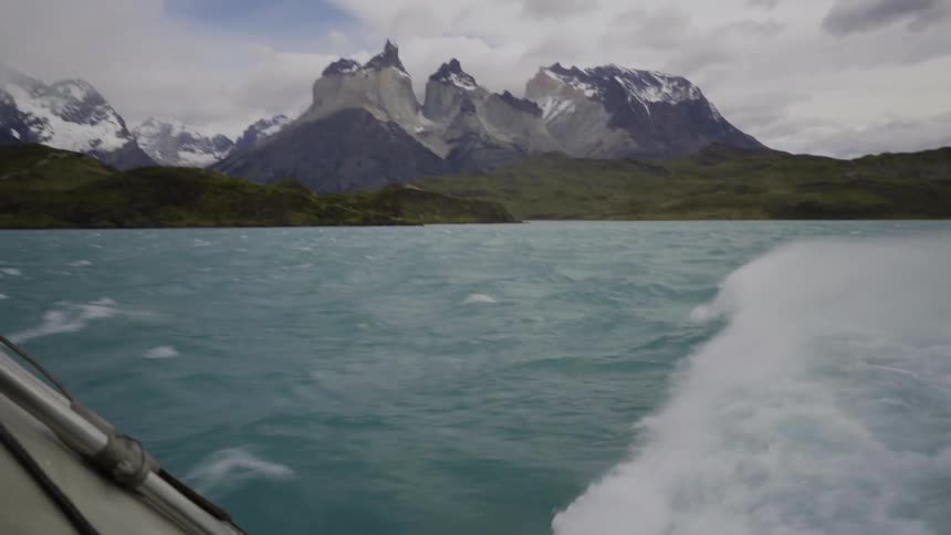 A boat is traveling in a lake by a mountain
