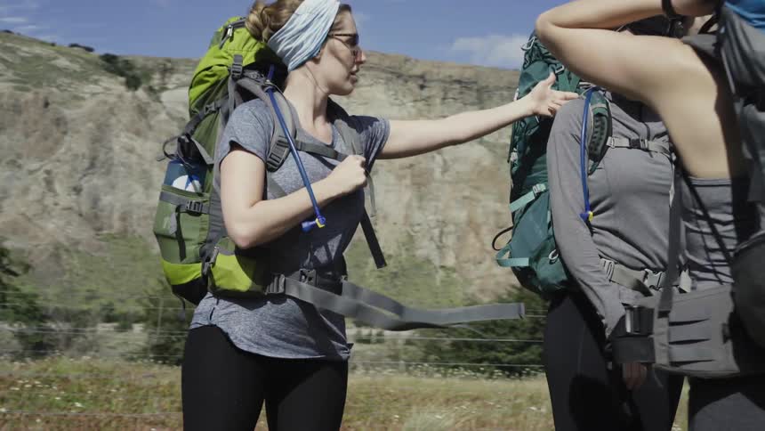 Three women wearing large backpacks talking in nature