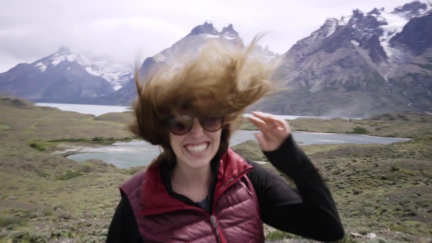 A woman smiles while wind blows her hair all around in the mountains