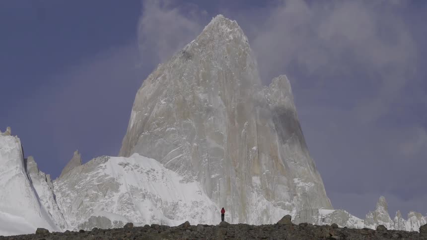 A hiker stands at the base of a rocky mountain