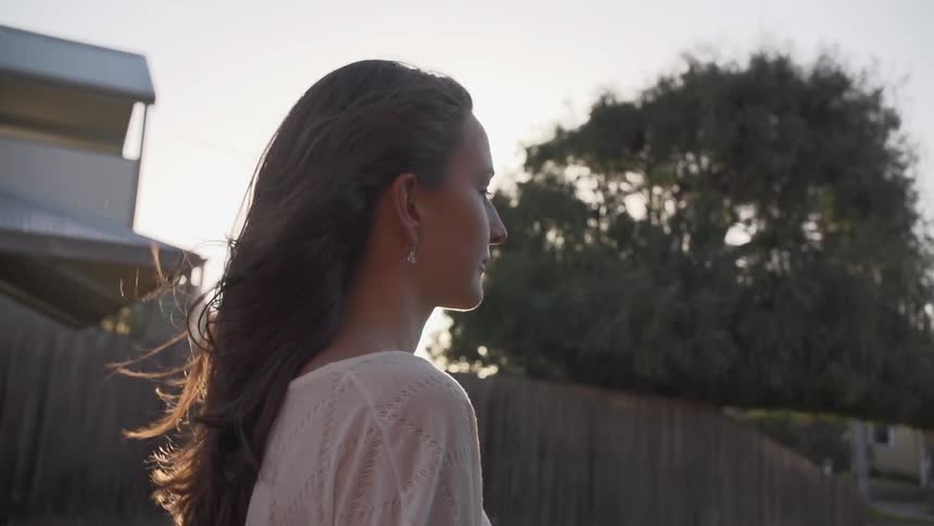 A tight shot of a young woman with brunette hair walking down a neighborhood street