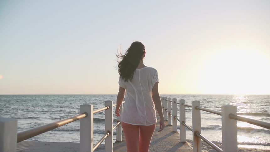 A woman walks down a pier towards the water