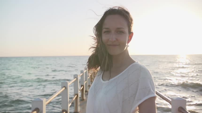 Woman walking down an ocean pier looking back and smiling
