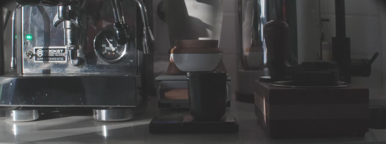 Coffee beans being poured into a container beside an espresso machine
