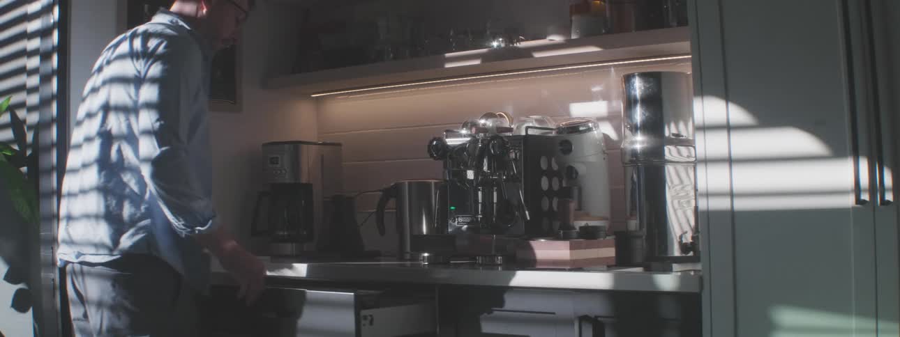 The man walks in and turns on the coffee machine