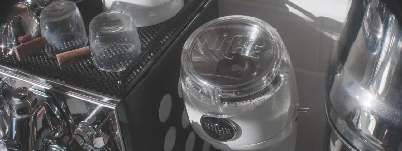 Closeup of a barista scooping coffee beans into a grinder in a well lit cafe