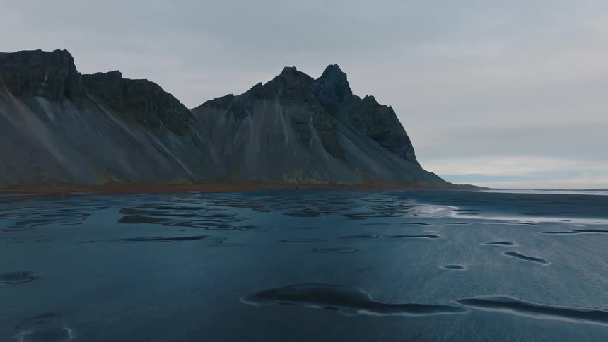Rocky mountain rises beside a blue lake under a cloudy sky
