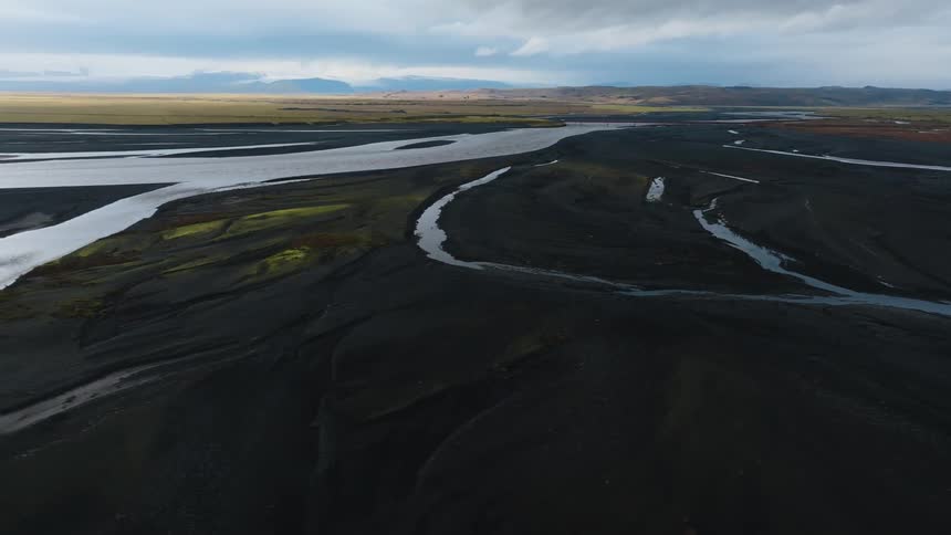 Braided rivers weave through dark volcanic terrain under a cloudy sky