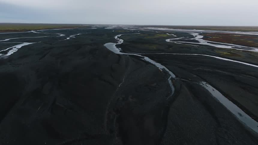 An open landscape stretches under the midday sun dotted with a series of gently flowing streams weaving through the terrain