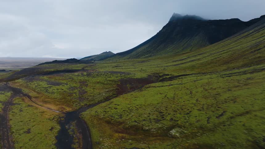 A mountain range covered in short grasses stretches beneath a cloudy sky its gentle slopes muted by the overcast light