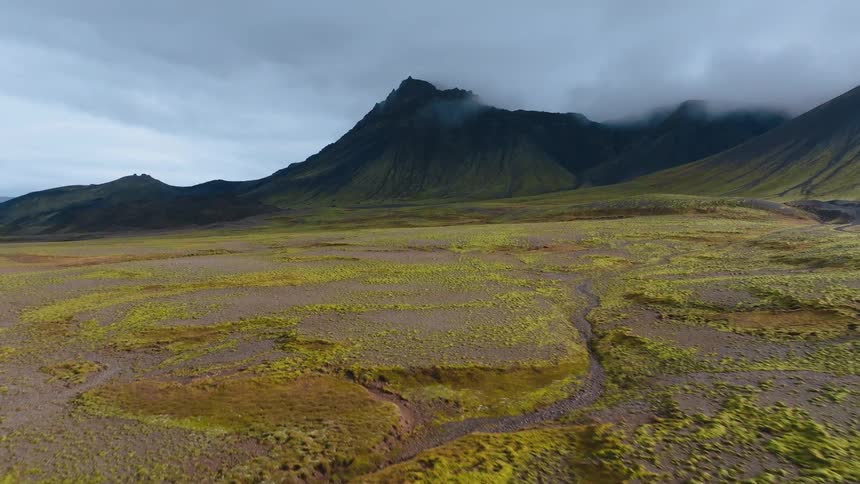 A vast moss covered plain towards a dark mountain shrouded in clouds