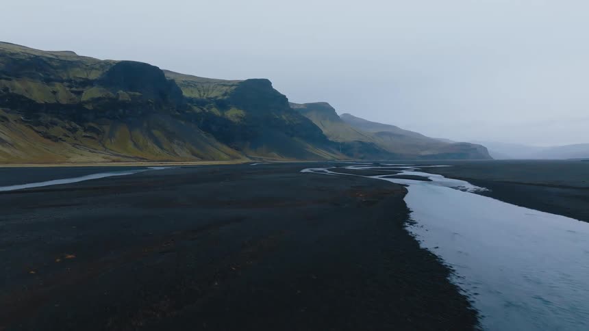 River winds through rocky terrain between steep mountains under cloudy sky revealing isolated and serene landscape