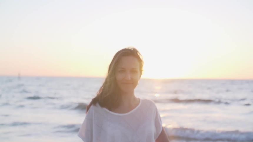 A woman smiles as she walks and turns by the shore